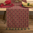 Festive red mistletoe table runner styled on a wooden dining table with napkins and Christmas place settings.