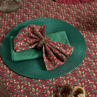 Festive table setting featuring a mistletoe print napkin in a decorative ring on a green placemat