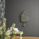 Jungle Green modern cuckoo clock styled on a dark grey wall above a lit candle