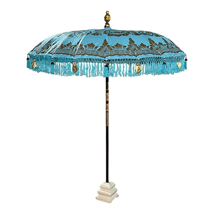 Bali sun parasol in light blue with gold painted patterns and fringe, shown standing in a white stone base