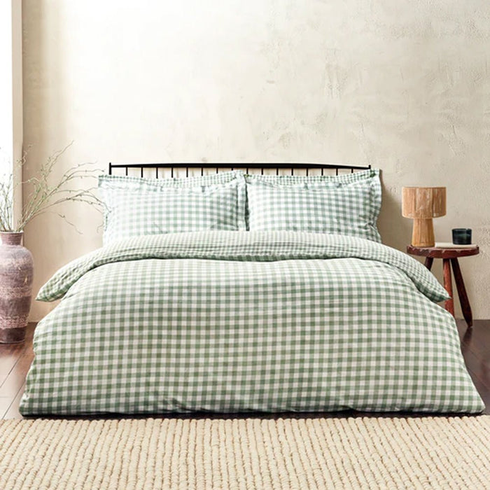 Forest green and white check duvet cover set styled on a dark metal bed frame with a rustic side table.