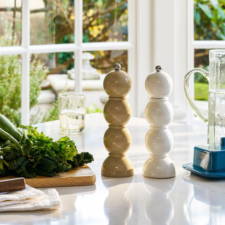 Cappuccino and white bobbin grinders styled on a marble kitchen worktop next to fresh greens and a butter dish