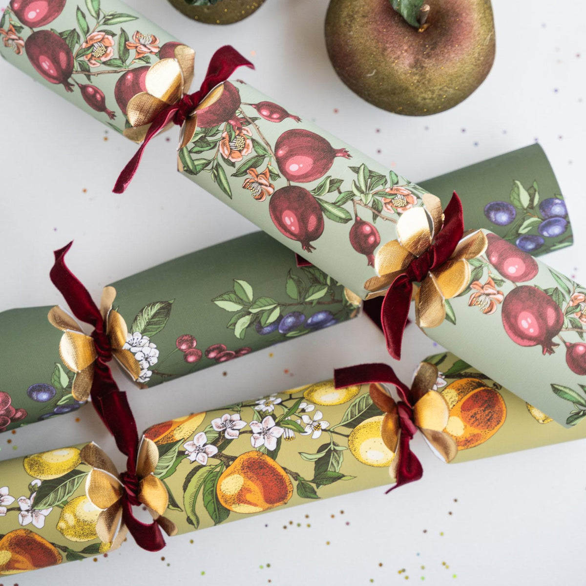 Vintage-style Christmas crackers with pomegranate and cherry patterns scattered on a white surface.