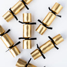 Gold Christmas crackers scattered on a white surface showing the black velvet ribbon details.
