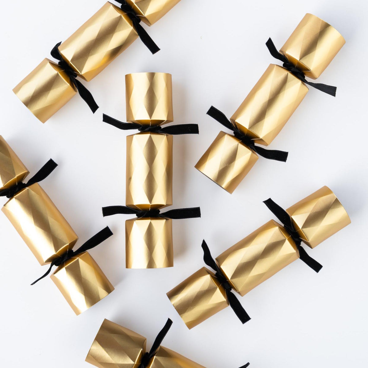 Gold Christmas crackers scattered on a white surface showing the black velvet ribbon details.