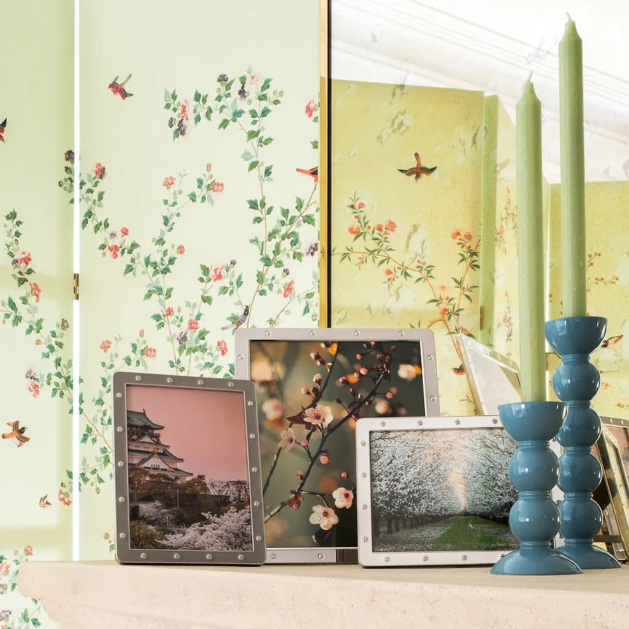 Pair of Chambray Blue bobbin candlesticks with green dinner candles styled on a mantelpiece with floral frames.
