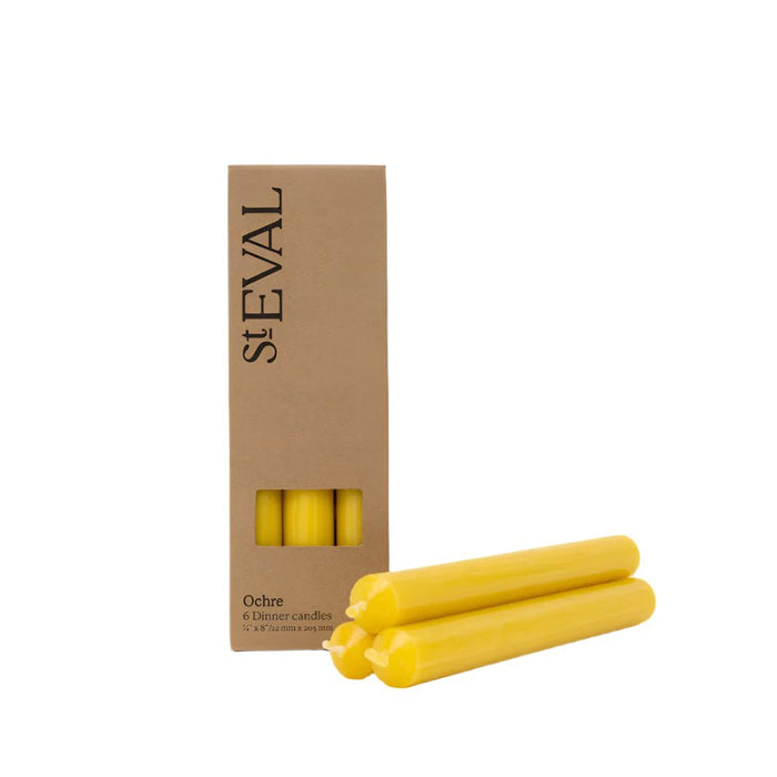Pack of six ochre yellow dinner candles next to their brown cardboard packaging