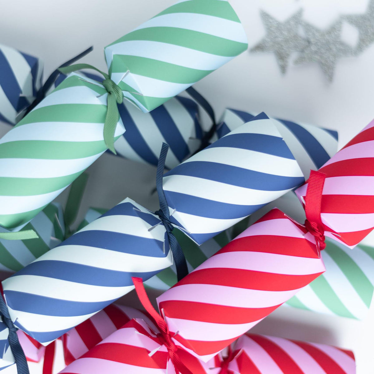 Close-up of diagonal striped Christmas crackers in blue, green, and red with matching ribbons.