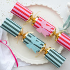Two striped Christmas crackers with pink and blue bows on a white plate.