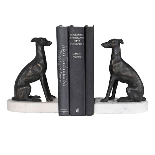 A pair of dark metal greyhound bookends on white marble bases holding three black books.