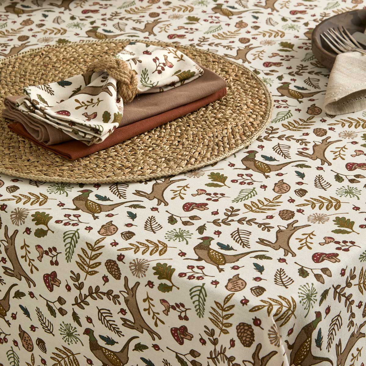 Woodland print napkins styled on a rustic place setting with a matching tablecloth and woven placemat.
