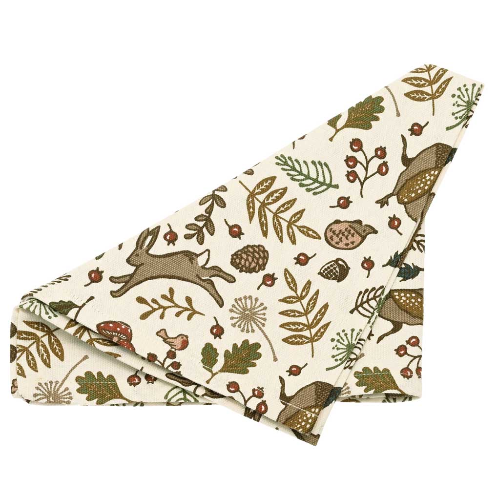 Into the Woods cotton napkin folded to show a print of hares, pheasants, and leaves in earthy tones.