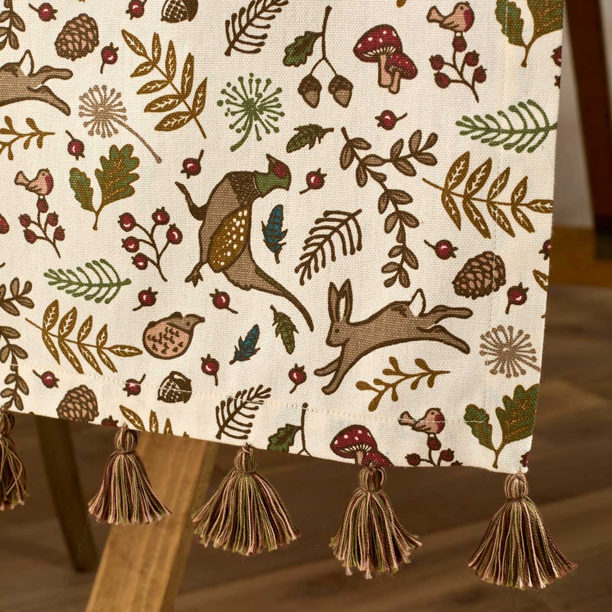 Close up of woodland print table runner showing hare, pheasant, mushroom and leaf motifs in autumn colours.