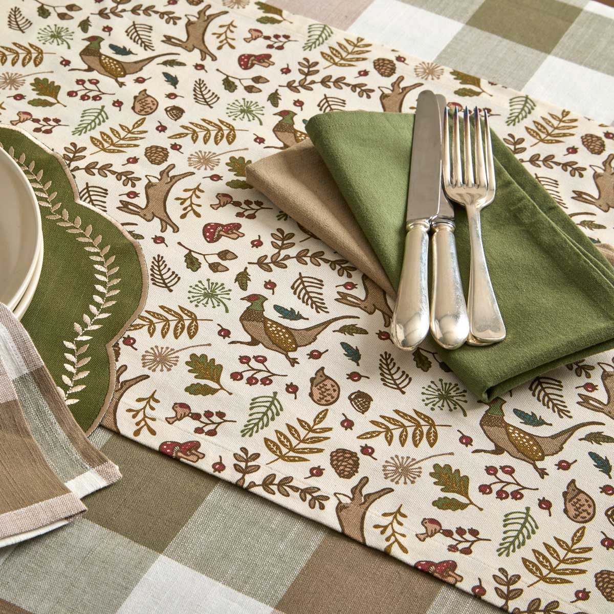 Overhead view of woodland table runner styled with green napkins and silver cutlery on a checked tablecloth.
