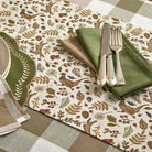 Overhead view of woodland table runner styled with green napkins and silver cutlery on a checked tablecloth.