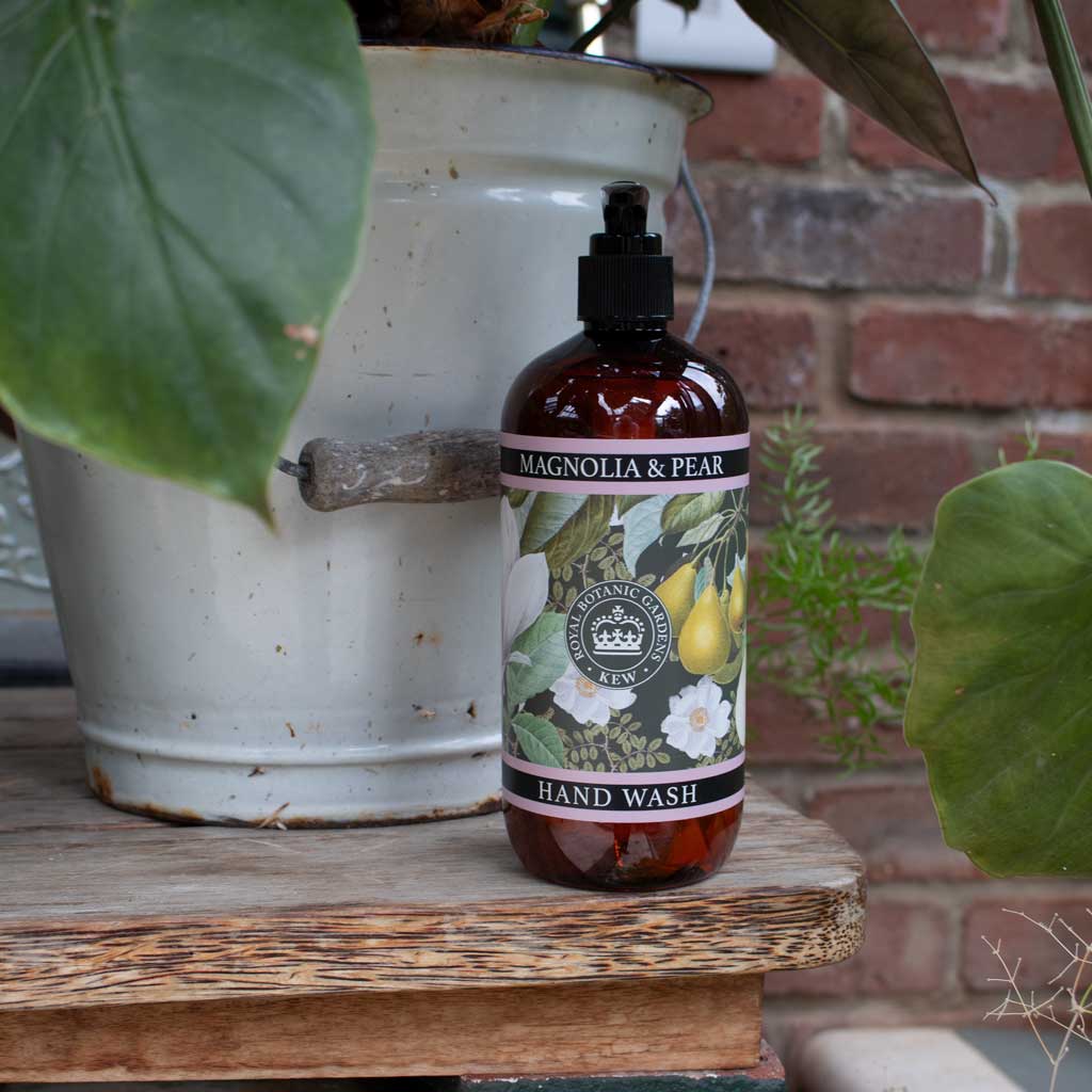 Lifestyle shot of the Kew Gardens Magnolia and Pear hand wash on a rustic wooden surface next to a garden pot.