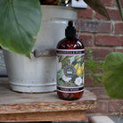 Lifestyle shot of the Kew Gardens Magnolia and Pear hand wash on a rustic wooden surface next to a garden pot.