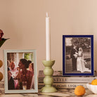 A gloss bobbin candlestick styled on a stack of books alongside framed photographs and an orange