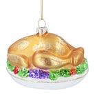 Golden glass roast turkey bauble on a white platter with green and purple garnishes and glitter accents.