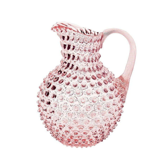 A soft pink crystal glass hobnail jug with a tapered handle against a white background.