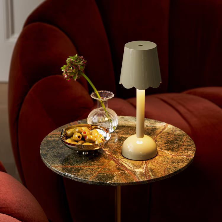 Sage green scalloped table lamp lit on a marble side table next to a velvet armchair