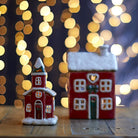 Small church tea-light holder and cottage styled on a wooden surface with festive bokeh lights