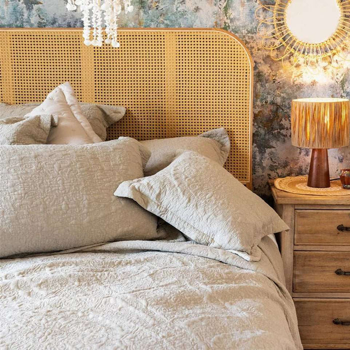 Parchment quilted bedspread styled on a bed with a rattan headboard and matching pillows
