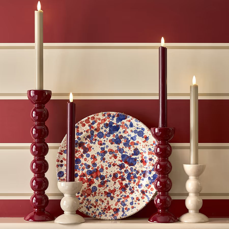 A collection of red and cream bobbin candlesticks in varying heights styled against a striped wall.