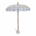 Full view of the white and gold Balinese sun parasol standing in a stone base against a white background.