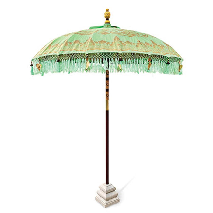 Full view of the Bali Sun Parasol in mint with gold leaf patterns and fringe on a wooden pole and stone base