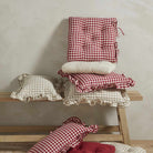 A stack of gingham cushions in red and beige tones styled on a wooden bench.