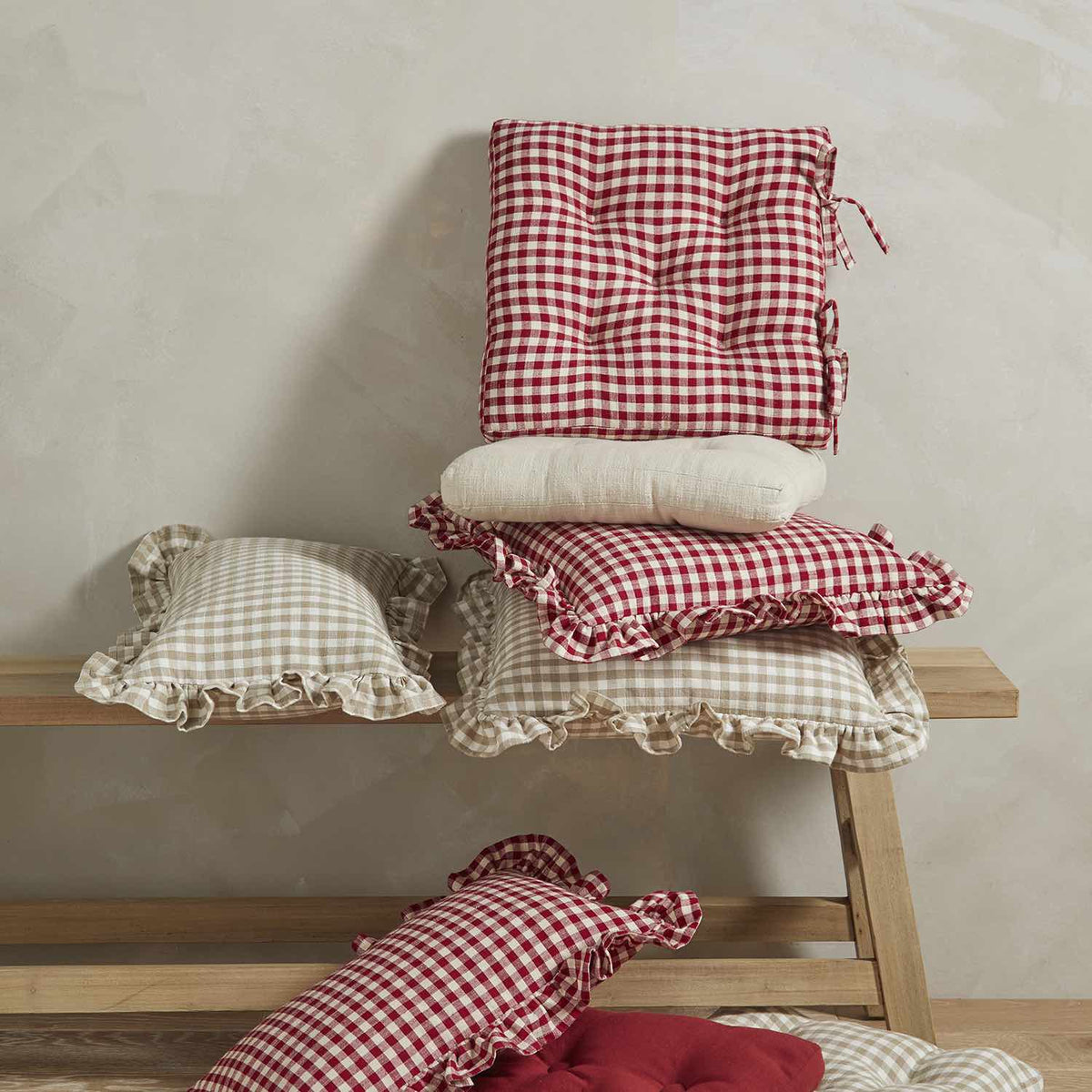 A stack of gingham cushions in red and beige tones styled on a wooden bench.