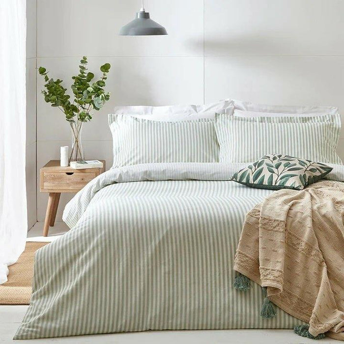 Hebden Eucalyptus green and white striped duvet cover set styled on a bed with a botanical leaf print cushion.