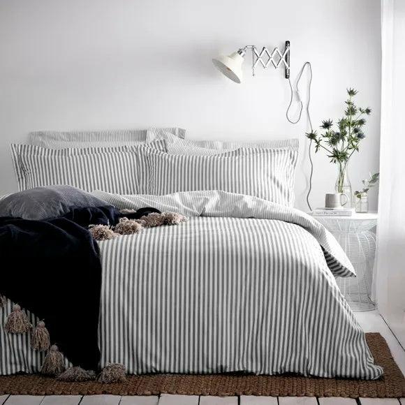 Hebden grey and white striped duvet cover set styled on a bed with dark throw and matching pillowcases