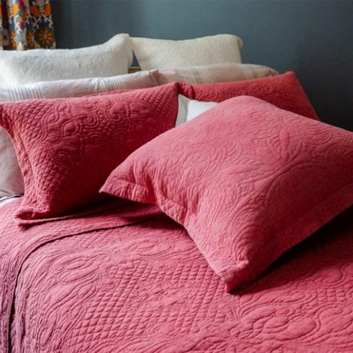 Close-up of a terracotta quilted bedspread and matching pillowcase showing the intricate circular stitching pattern.